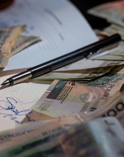 Pióro wieczne leżące na dokumentach finansowych w otoczeniu polskich banknotów, symbolizujące przygotowanie wniosku o upadłość konsumencką 2026 i początek drogi do oddłużenia.
