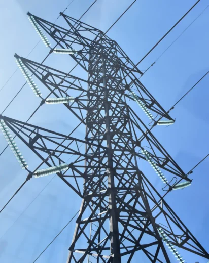 Widok z dołu na potężny metalowy słup linii wysokiego napięcia na tle błękitnego nieba, ilustrujący infrastrukturę przesyłową, za którą właścicielom gruntów przysługuje zapłata za słupy na działce w formie odszkodowania.