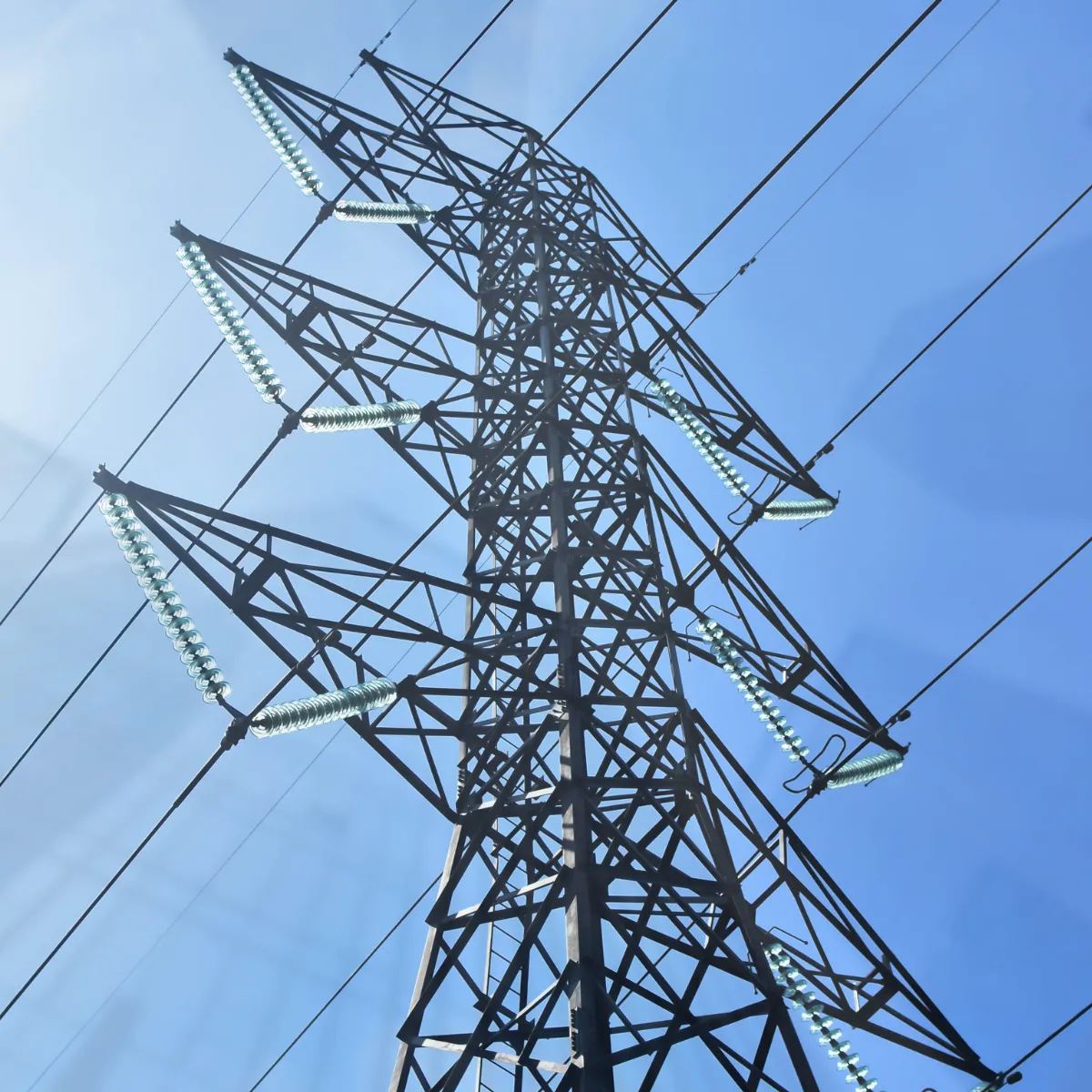 Widok z dołu na potężny metalowy słup linii wysokiego napięcia na tle błękitnego nieba, ilustrujący infrastrukturę przesyłową, za którą właścicielom gruntów przysługuje zapłata za słupy na działce w formie odszkodowania.