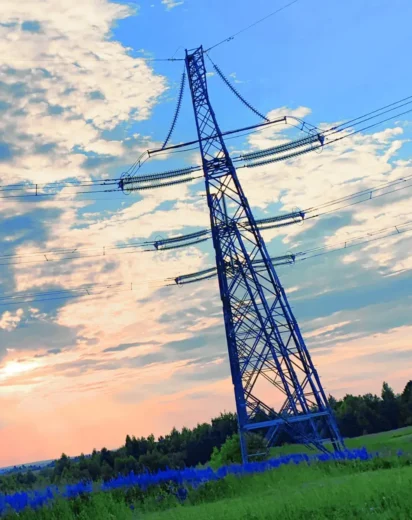 Wysoki słup energetyczny na prywatnej działce o zachodzie słońca. Ilustracja do poradnika o prawnych możliwościach żądania usunięcia urządzeń przesyłowych przez właściciela gruntu.