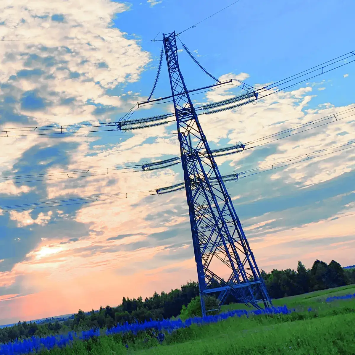 Wysoki słup energetyczny na prywatnej działce o zachodzie słońca. Ilustracja do poradnika o prawnych możliwościach żądania usunięcia urządzeń przesyłowych przez właściciela gruntu.