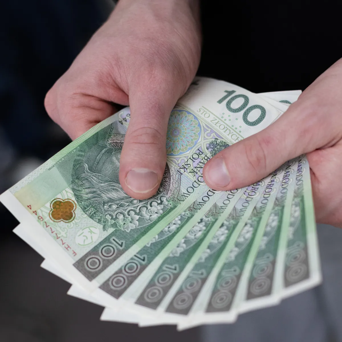 Mężczyzna trzymający w dłoniach banknoty 100 złotych po ogłoszeniu planu spłaty po upadłości.