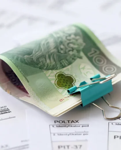 Plik banknotów 100 zł spięty niebieskim klipsem na dokumentach finansowych. Ilustracja do poradnika o sankcji kredytu darmowego i odzyskiwaniu kosztów bankowych w 2026 roku.