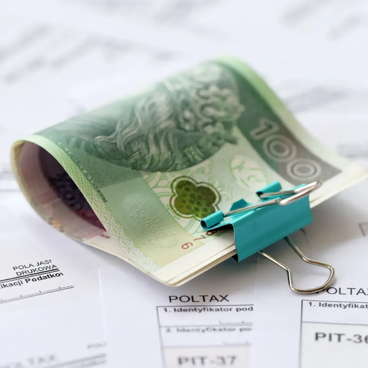 Plik banknotów 100 zł spięty niebieskim klipsem na dokumentach finansowych. Ilustracja do poradnika o sankcji kredytu darmowego i odzyskiwaniu kosztów bankowych w 2026 roku.