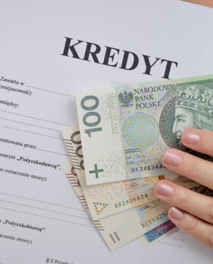 Dłoń trzymająca polskie banknoty na tle umowy pożyczki, ilustrująca temat: upadłość konsumencka a chwilówki i kredyty gotówkowe.