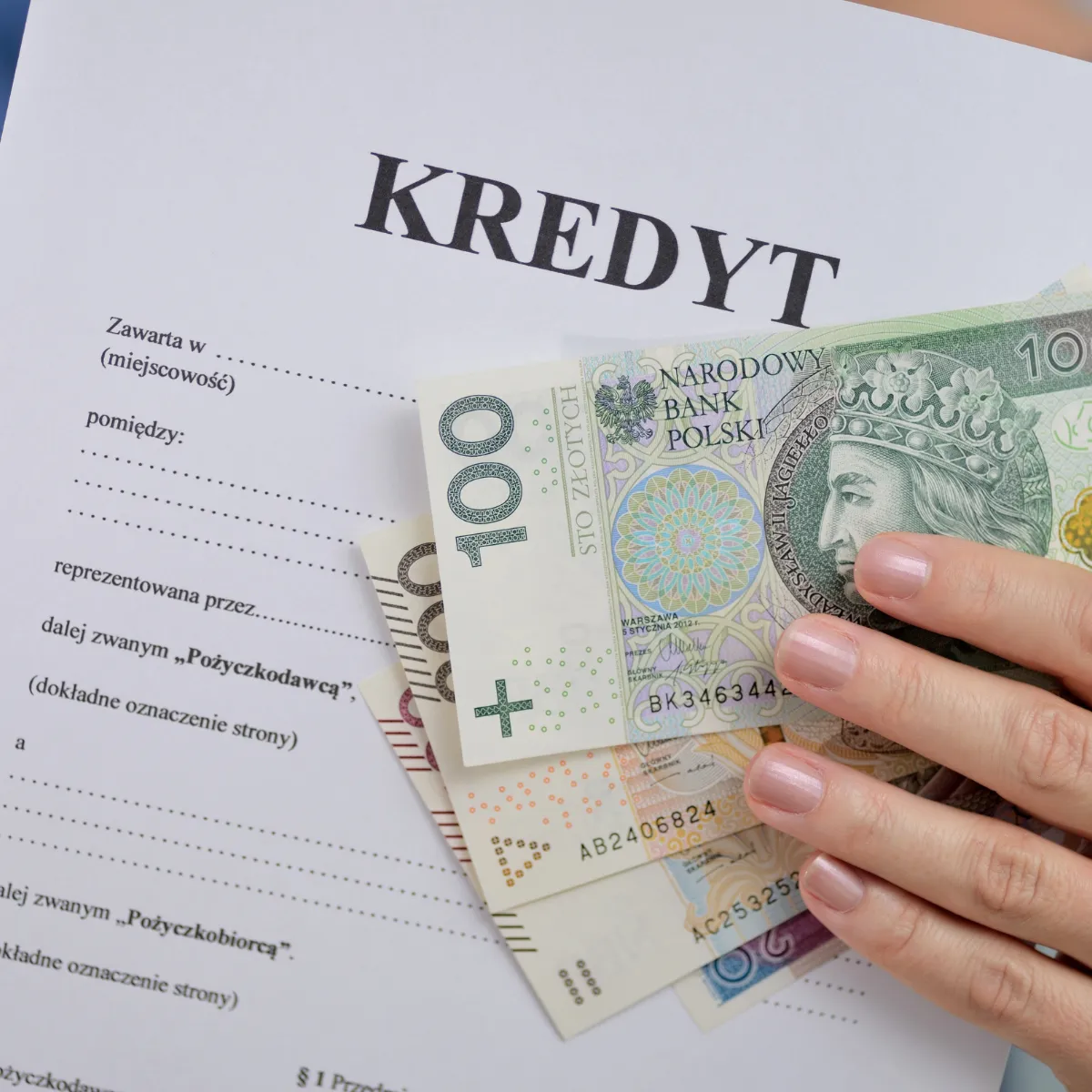 Dłoń trzymająca polskie banknoty na tle umowy pożyczki, ilustrująca temat: upadłość konsumencka a chwilówki i kredyty gotówkowe.